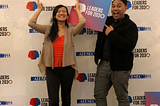 A man and woman holding props in front of a backdrop of Leaders for 2030