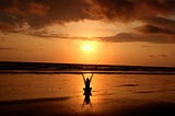 Image of a woman sitting cross-legged and raising her hand to the sunset on the beach