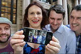 Four people stand in front of the Apple Store in Brisbane’s Queen St, one holds up a cellphone which displays an image of the four.