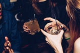 duas mulheres se divertindo numa festa com bebidas na mão. a imagem está cortada e mostra apenas o sorriso de uma delas.