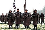 Two color guards and color bearers of the Japanese-American 442d Combat Team, stand at attention, while their citations are read. They are standing on ground in the Bruyeres area, France, where many of their comrades fell.