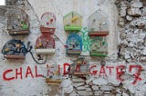 Colored birdcages mounted on a wall, inscribed CHALKIDA GATE 7 in red.