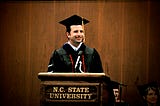 The author, wearing doctoral regalia and a graduation cap, stands behind an N.C. State University podium while giving a commencement address in 2009, the same year he earned his PhD.