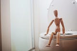 wooden figurine sits on edge of toilet bowl