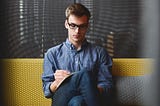 Young man sitting on a couch writing on a notebook.