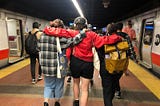 Mack Lawrence and two friends walking on a subway platform in New York City. Image taken from the back.