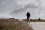 Person in black jacket and beige shorts walking under a grey sky