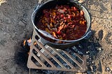Cast iron pot of campout chili over a fire pit