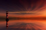 a lighthouse silhouetted against an orange and red sunset