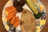 A plate with falafel (chickpea balls), carrots, pickle, whole wheat bread, and chutney.