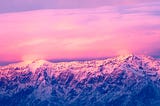 Mountain range at sunset under a brilliant pink sky.