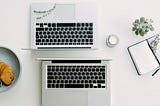 Two Macbooks standing back to back, next to a bowl with cookies and a notebook.