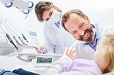 Stock image of a child in a dentist’s chair with a dentist and dental hygienist smiling while conversing with the child.