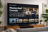 TV screen shows “Masterchef Canada” episode with two chefs, kitchen background. Menu below includes options like “Top Critic.” Room has plants.