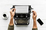 An antique typewriter with a piece of paper, a coffee cup and a phone that sits on a desk.