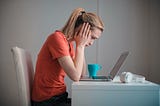 Distressed woman is leaning over laptop sitting at a desk