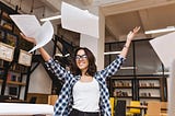 Smiling brunette wearing glasses throwing paper