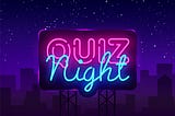 A neon sign that says “Quiz Night”, over a cityscape at night.