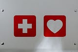 image shows a white medical cross on a red background and a white heart on a red background