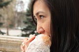A white woman with dark hair eating a sandwich outdoors