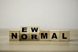 Wooden blocks with the phrase new normal slightly tilted upward in black lettering.