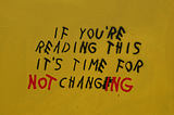 Graffiti on a yellow wall reading “If you’re reading this it’s time for change,” with the word “NOT” added and “CHANGE” altered to “CHANGING” in red paint, symbolizing resistance to unnecessary redesigns.