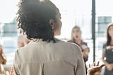 Black girl looking onto a room of coworkers, like she’s giving a presentation