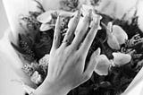 a black and white image of a woman’s hand wearing a wedding ring over a bouquet of flowers.