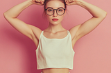 article key visual with a young woman with glasses, looking nerdy, showing a muscle, demonstrating a recent victory, feeling glorious. Key colors “e11a72. Studio shot, hyper-realistic, photo realistic, canon D118 shot,, flat pale pink background,