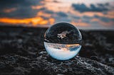 Glass globe sitting on rocks reflecting the sunset but upside down.