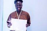 A young african adult wearing brown and holding a Macbook Air.
