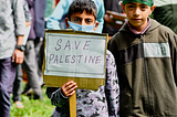 A boy holds a handwritten sign that says “Save Palestine.”