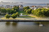 Aerial photo of MIT’s Great Dome with a lawn, trees, and a river in the foreground.