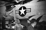 Military man smiling standing in front of fighter jet.