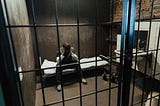 A young man sits in a prison cell, head in hands.