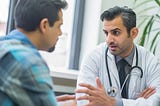 A focused doctor in a white coat discusses medical concerns with a male patient.