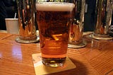 a full pint glass of beer sitting on a wooden bar