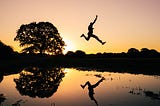 man jumping over water at sunset