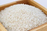 Zdjęcie małej, drewnianej skrzynki pełnej ziaren białego ryżu
