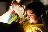 Boy reading The Very Hungry Caterpillar to a girl by flashlight.