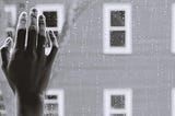 Black and white filter of a hand pressed against a window with raindrops on it.