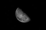 a third quarter half moon in greyscale on a black sky background with sparse tiny stars sprinkled lightly around