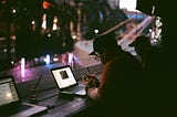 Young guys sitting at a counter with laptops looking out window at city in evening