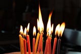 Image of about a dozen lit birthday candles.
