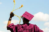 Arizona State University graduate wearing maroon cap and gown, twirling gold tassels in left hand.