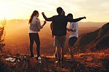 four friends dancing on a mountain at sunset