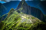 Photo of very green mountain-ridge citadel Machu Picchu in Peru against dark mountains under a cloudy sky.