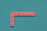 A solid background with plastic squares that have a single letter on each of the squares arranged to spell “Finally Free”.