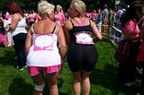 Two women sticking out their butts at a Race for Life UK event with other participants in the background.