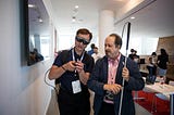 A visually impaired man wearing a Magic Leap AR device examines a controller, while another man looks on holding his white cane.